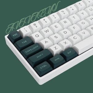 May include: A white mechanical keyboard with dark green keycaps. The keycaps have white lettering and include keys such as ESC, TAB, CAPS LOCK, SHIFT, CTRL, WIN, and ALT.