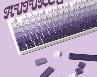 May include: A white mechanical keyboard with purple and gray keycaps. The keyboard has a gradient of colors from white to purple. The keycaps are arranged in a standard QWERTY layout. The keyboard is surrounded by individual keycaps, including a purple 'CapsLk' keycap and a gray 'Tab' keycap.