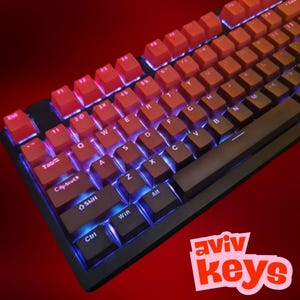 May include: A mechanical keyboard with red and brown keycaps, featuring a gradient color scheme. The keyboard has a black frame and blue under-key lighting. The brand name "aviv Keys" is displayed in a pink and white logo.