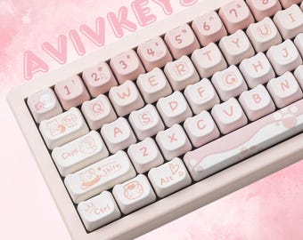 Puede incluir: Un teclado mecánico rosa y blanco con teclas personalizadas. El teclado tiene un marco rosa claro y teclas con una mezcla de teclas blancas y rosas. Las teclas presentan ilustraciones personalizadas y el texto "AVIVKEYS" se muestra en la parte superior.