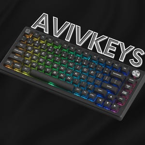 May include: A black mechanical keyboard with backlit keys displaying a rainbow gradient. The keyboard has a black wrist rest and a silver knob. The text "AVIVKEYS" is displayed above the keyboard.