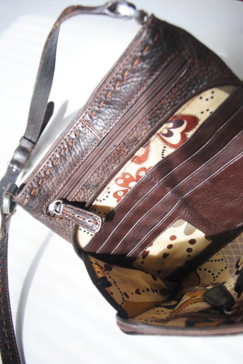May include: A brown leather crossbody purse with a zippered closure and multiple interior pockets. The purse has a floral patterned lining.