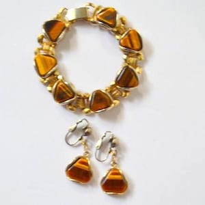 May include: A gold-tone link bracelet featuring triangular tiger's eye stone inlays and a matching pair of clip-on drop earrings. Each piece of jewelry showcases the distinct brown and golden striped pattern of the polished tiger's eye stones.