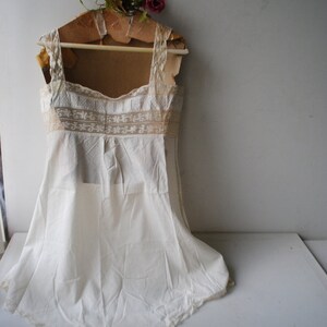 May include: A white cotton slip with lace trim and a scalloped hem. The slip is hanging on a wooden hanger with a floral decoration.
