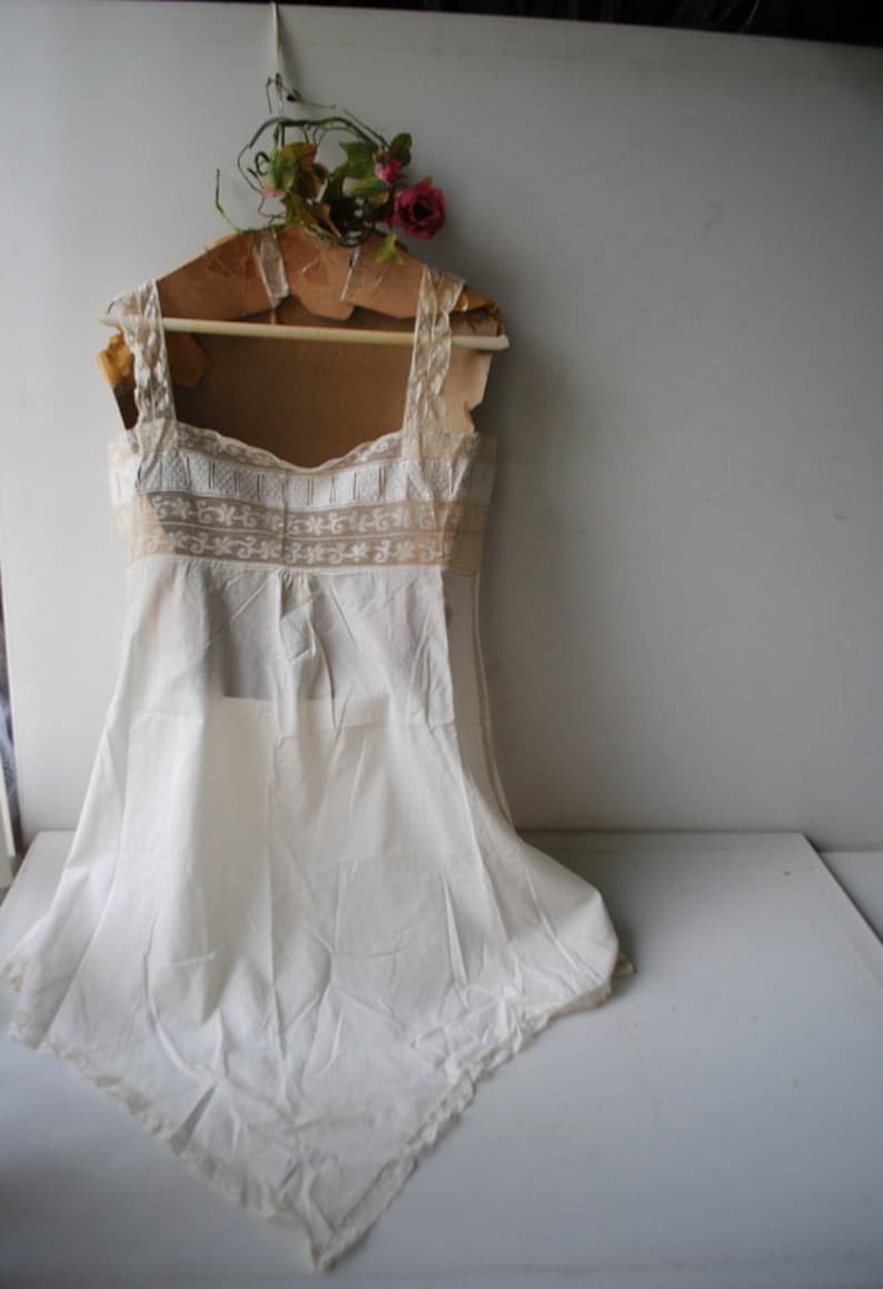 May include: A white cotton slip with lace trim and a scalloped hem. The slip is hanging on a wooden hanger with a floral decoration.
