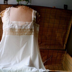 May include: A white lace-trimmed slip dress with a delicate floral pattern, displayed in an antique wooden suitcase.