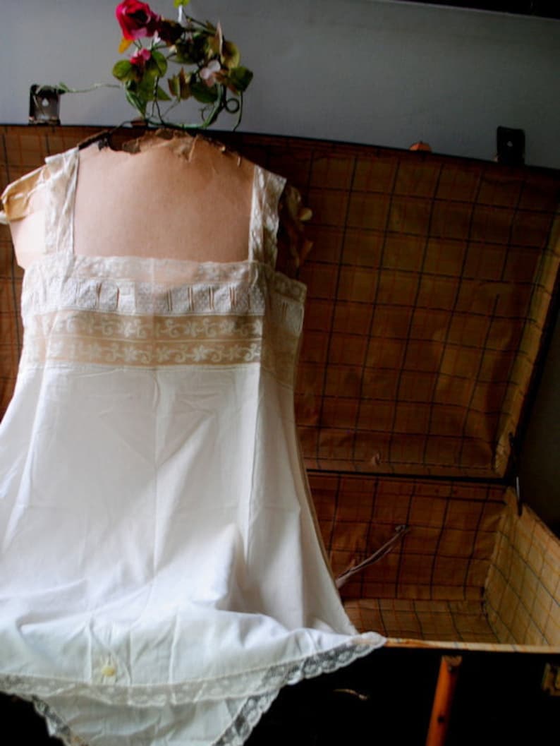 May include: A white lace-trimmed slip dress with a delicate floral pattern, displayed in an antique wooden suitcase.