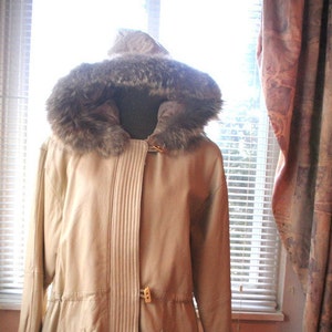 May include: A beige leather jacket with a fur-trimmed hood. The jacket has a zipper closure and a belt at the waist.