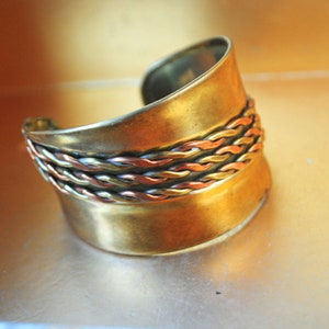 Brutalist vintage 70s, bold gold tone metal, asymmetric cuff, wide bracelet with a woven details.Size 7.