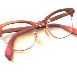 May include: A pair of vintage brown cat-eye glasses with gold accents. The glasses have clear lenses and a red interior.