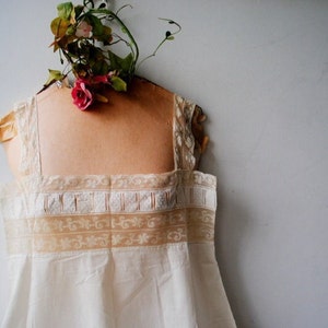 May include: A white cotton slip with delicate lace trim. The slip is on a dress form with a floral decoration.