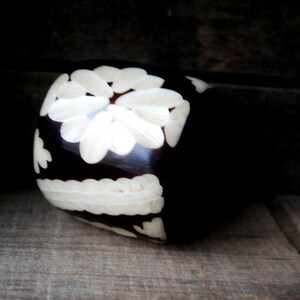 May include: A dark brown wooden ring with a white floral design carved into the surface.