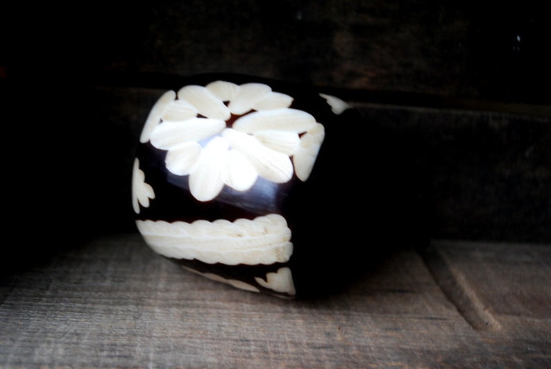 May include: A dark brown wooden ring with a white floral design carved into the surface.