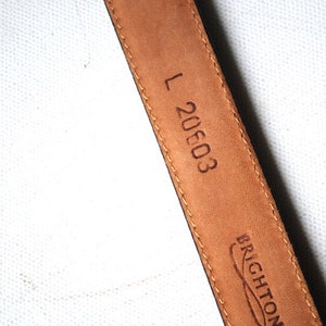 Peut inclure: Ceinture en cuir marron avec une boucle noire et le texte "L 20603" et "BRIGHTON" en relief au dos.