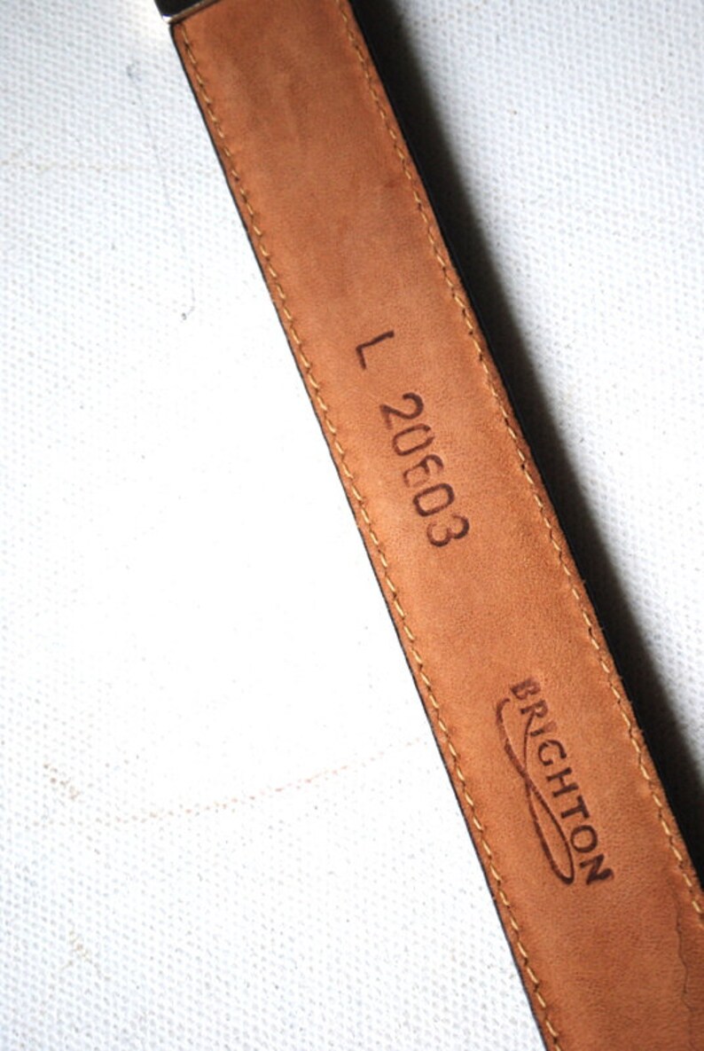 Peut inclure: Ceinture en cuir marron avec une boucle noire et le texte "L 20603" et "BRIGHTON" en relief au dos.