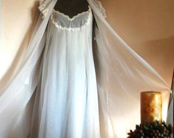 May include: A floor-length white nightgown and matching sheer robe set. The nightgown features a sweetheart neckline with delicate white lace trim and small pink floral accents. The robe has wide, flowing sleeves with matching lace detailing.