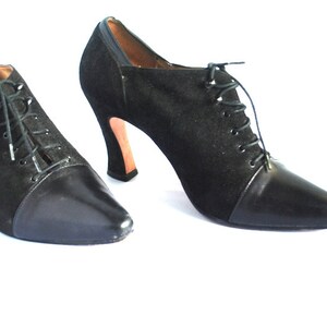 May include: A pair of black suede and leather ankle boots with lace-up fronts and high heels.