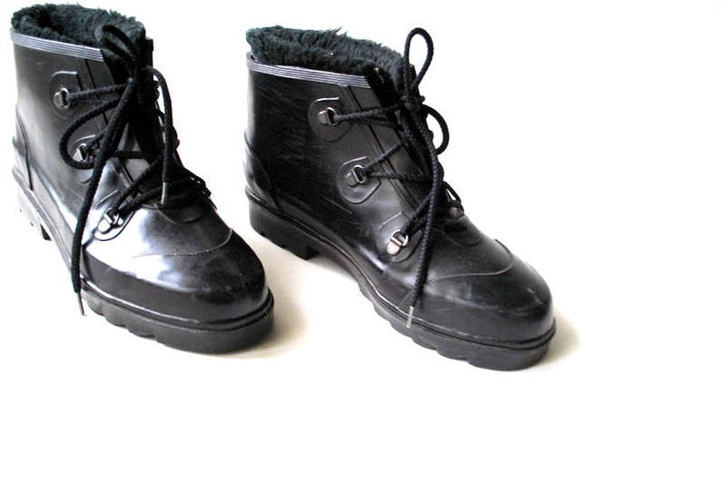 May include: A pair of black, lace-up boots with a shiny finish. The boots have a faux fur lining visible at the top and a sturdy, ridged sole. The laces are black, and the boots appear to be made of a rubber-like material.