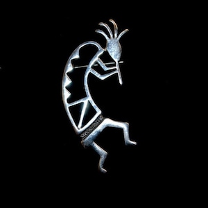 May include: A silver-toned Kokopelli figurine pendant, a traditional Native American symbol of fertility and music, with intricate details and a black stone inlay.
