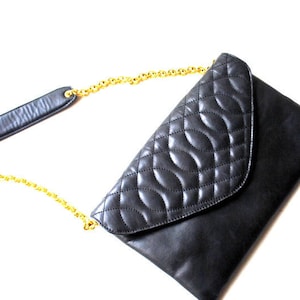 May include: A black quilted leather clutch bag with a gold chain strap.