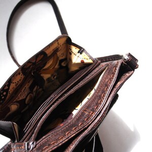 May include: A brown leather purse with a zipper closure and a patterned fabric lining. The purse has a long strap and multiple compartments.