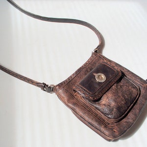 May include: A brown leather crossbody bag with a flap closure and a silver buckle. The bag has a small pocket on the front.