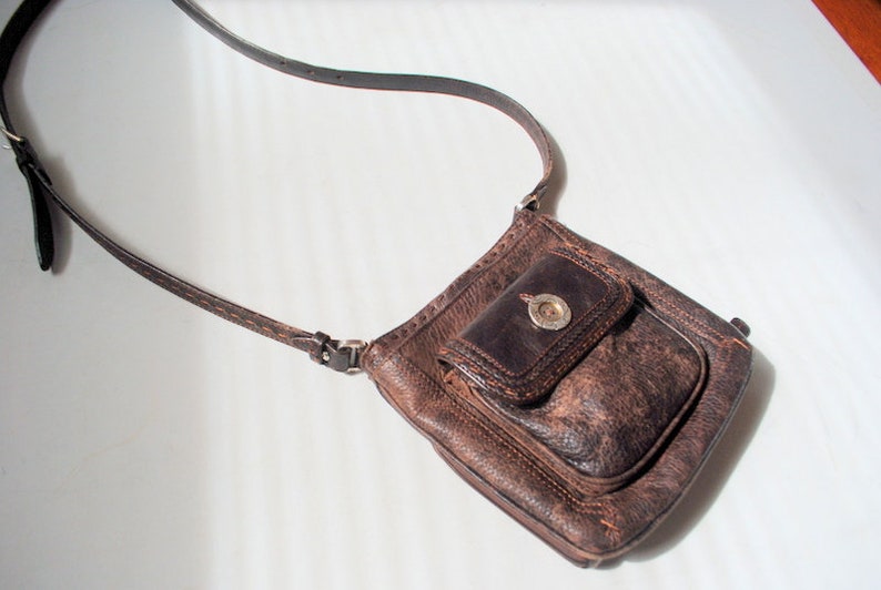 May include: A brown leather crossbody bag with a flap closure and a silver buckle. The bag has a small pocket on the front.