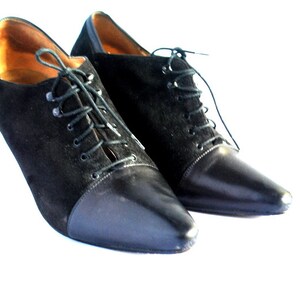 May include: A pair of black suede and leather heeled shoes with lace-up closures. The shoes have a pointed toe and a high heel.