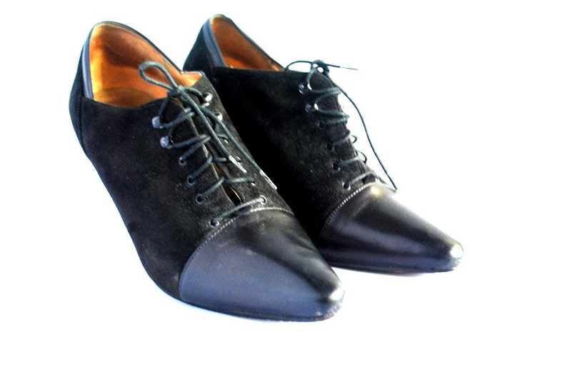 May include: A pair of black suede and leather heeled shoes with lace-up closures. The shoes have a pointed toe and a high heel.