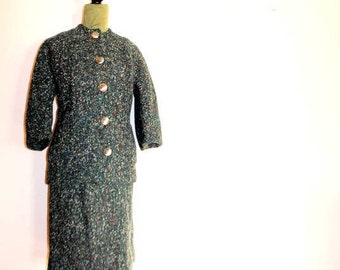 May include: A green tweed skirt suit with a button-up front and a fitted skirt. The suit is on a mannequin.