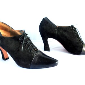 May include: A pair of black suede ankle boots with a pointed toe and lace-up closure. The boots have a chunky heel and a leather cap toe.