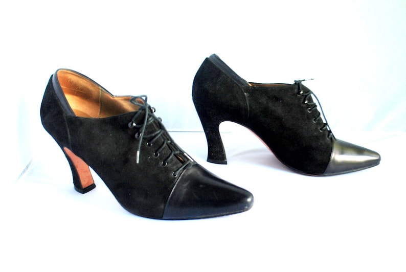 May include: A pair of black suede ankle boots with a pointed toe and lace-up closure. The boots have a chunky heel and a leather cap toe.
