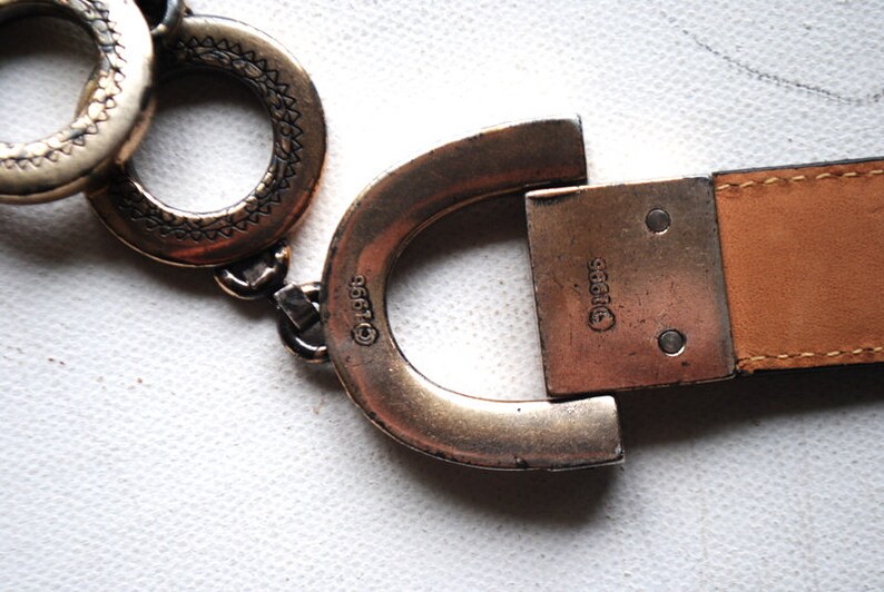 Peut inclure: Une boucle de ceinture argent&eacute;e avec une sangle en cuir. La boucle est en forme de fer &agrave; cheval et porte le texte "&copy;1995" d'un c&ocirc;t&eacute; et "&copy;1995" de l'autre.