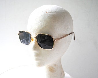 May include: Gold aviator sunglasses with dark lenses. The sunglasses are on a white mannequin head.