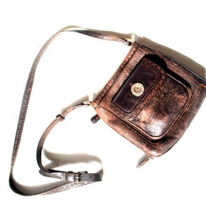 May include: A brown leather crossbody bag with a flap closure and a single pocket on the front. The bag has a worn, distressed look and a silver-toned buckle.