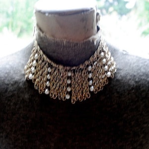 May include: A gold chain necklace with white pearl accents. The necklace is a choker style and has a fringe design.