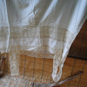 May include: A white cotton garment with lace trim, hanging inside a wooden trunk.