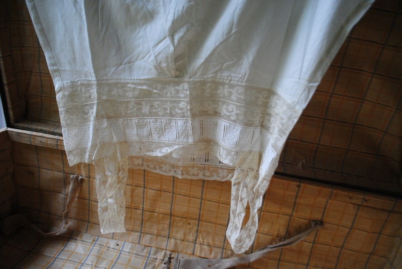 May include: A white cotton garment with lace trim, hanging inside a wooden trunk.