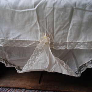 May include: White cotton slip with lace trim. The slip has a gathered waist and a button closure at the center back.