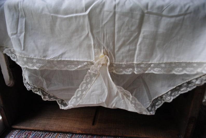 May include: White cotton slip with lace trim. The slip has a gathered waist and a button closure at the center back.