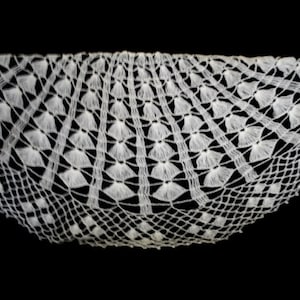 Pode incluir: Doily de renda branca de crochê com uma borda festonada e um delicado padrão floral.