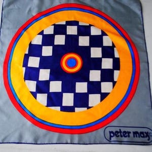 Könnte beinhalten: Peter Max Seidenschal mit einem zentralen Design aus konzentrischen Kreisen in Rot, Gelb und Blau, die ein blau-weißes Schachbrettmuster umgeben. Der Schal hat einen hellgrauen Rand und das Peter Max Logo.