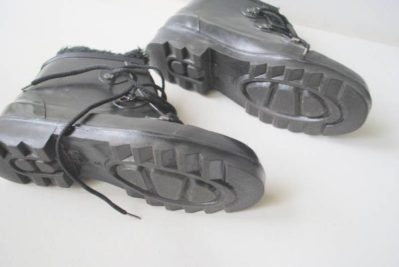 May include: A pair of black winter boots with chunky, textured soles. The boots feature laces and a faux fur lining at the top. They are made from a glossy material and are designed for cold weather conditions.
