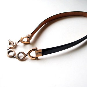 Peut inclure: Une ceinture en cuir noir avec une boucle dor&eacute;e et un d&eacute;tail de cha&icirc;ne. La boucle pr&eacute;sente un motif d&eacute;coratif.