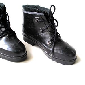 May include: A pair of black, lace-up boots with a shiny finish. The boots have a faux fur lining visible at the top and a sturdy, ridged sole. The laces are black, and the boots appear to be made of a rubber-like material.