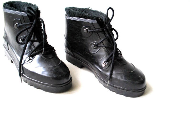 May include: A pair of black, lace-up boots with a shiny finish. The boots have a faux fur lining visible at the top and a sturdy, ridged sole. The laces are black, and the boots appear to be made of a rubber-like material.