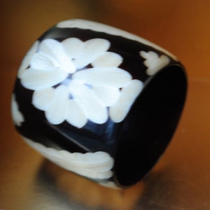 May include: A black bangle bracelet with white floral designs. The bracelet is made of a smooth, hard material.