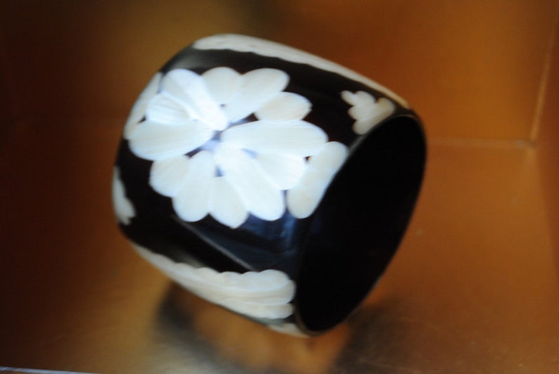 May include: A black bangle bracelet with white floral designs. The bracelet is made of a smooth, hard material.