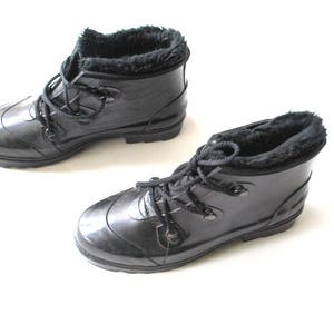 May include: Two black, glossy rain boots with faux fur lining and lace-up fastenings. The boots are displayed on a white background, highlighting their sleek design and practical features for wet weather conditions.