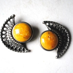 May include: A pair of silver earrings with a crescent moon design and a yellow amber stone in the centre of each earring.